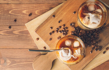 Glasses of cold brew with milk and coffee beans on wooden table