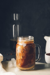 Mason jar with cold brew coffee and milk on board against dark background