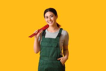 Asian female plumber with pipe wrench on yellow background