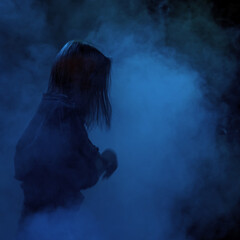 A girl with long hair in smoke in the spotlight. Low key. Soft focus