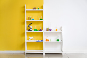 Shelving unit with different laboratory glassware and microscope near color wall