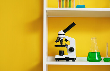 Shelving unit with different laboratory glassware and microscope near yellow wall
