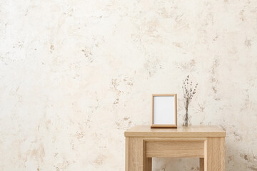 Obraz na płótnie Canvas Blank frame and vase with flowers on table near light wall