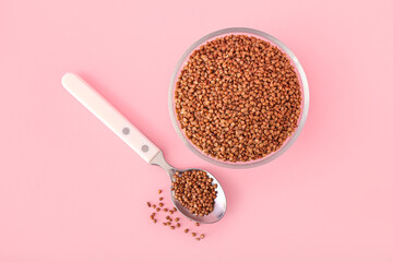 Glass bowl and spoon with buckwheat grains on pink background