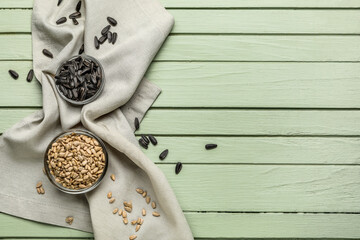 Bowls with sunflower seeds and napkin on green wooden background