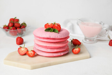 Board with tasty pink pancakes and strawberry on table