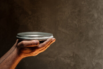 Male hands holding empty plate on dark background, lack of food, hunger concept. - obrazy, fototapety, plakaty