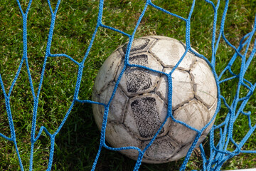 old soccer ball in the net on the background of grass soccer field. Summer sunny day