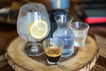 cold iced black brew coffee mixed lemon juice and lemon slices in a glass with pieces of ice on a wooden table, natural light, fresh summer drink in the morning