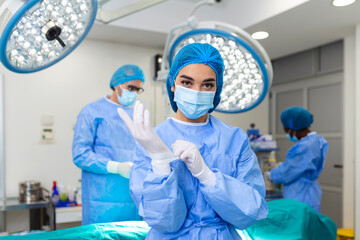 Portrait of beautiful female doctor surgeon putting on medical gloves standing in operation room....