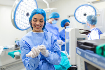 Portrait of beautiful female doctor surgeon putting on medical gloves standing in operation room. Surgeon at modern operating room