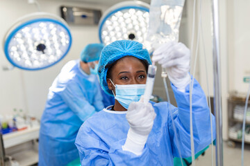African american female Doctor in the operating room putting drugs through an IV - surgery concepts