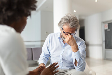 Female doctor reassuring supporting senior adult patient in hospital. Kind caring young woman nurse or caregiver helping older retired man talking, giving comfort, expressing care concept.