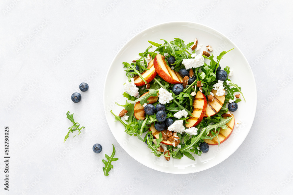 Poster peach, blueberry and arugula fresh fruit salad with cheese and almond nuts, top view