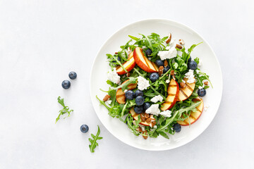 Peach, blueberry and arugula fresh fruit salad with cheese and almond nuts, top view