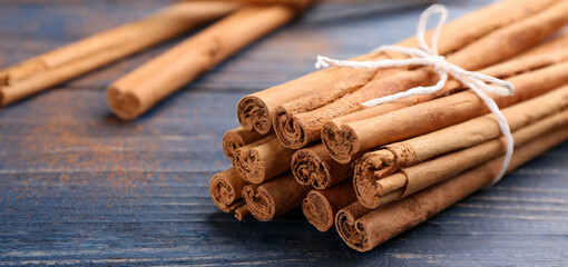 Aromatic cinnamon sticks on blue wooden table, closeup. Banner design - Powered by Adobe