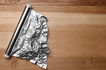 Roll of aluminum foil on wooden table, top view. Space for text