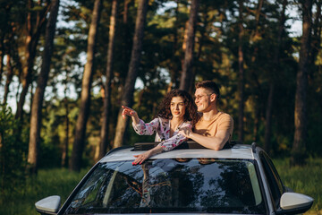 Happy couple sitting on top of minivan roof at sunset - Young people having fun on spring vacation traveling around the world - Travel,love and holiday concept - Focus on faces