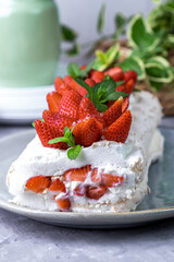 Meringue roll with strawberry filling and whipped cream. Summer dessert decorated with strawberries and mint on a gray background