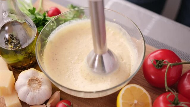 Making Caesar salad sauce - mixing grated parmesan cheese and olive oil in glass bowl with blender
