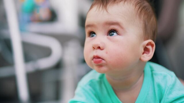 Sweet adorable baby with cute plump cheeks looks up. Portrait of a lovely curious toddler close up. Blurred backdrop.