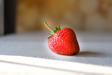 One red strawberry is placed on a wooden table.