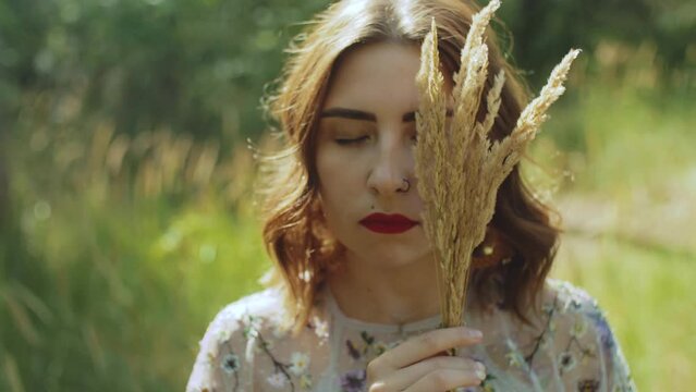 Close-up portrait of an attractive woman with closed eyes and a bouquet of spikelets in her hands near the face, slow motion shot.