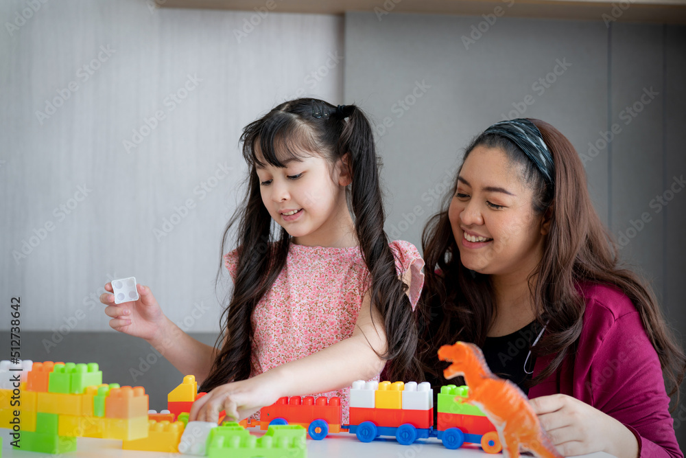 Wall mural Asian family mother and little asian girl smiling playing with toy build blocks at home. 