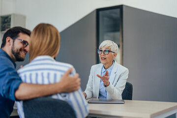 Close up of an elegantly dressed insurance agent, being in her office, talking to a young couple.