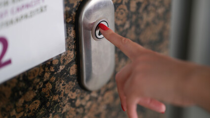 Female finger with red manicure pressing elevator button closeup