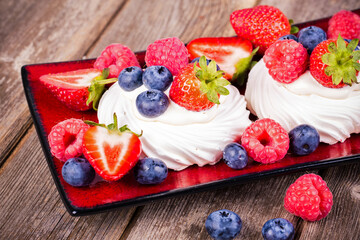 Summer fruit pavlovas on red platter, with strawberries, blueberries and raspberries. 
