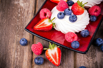 Summer fruit pavlovas on red platter, with strawberries, blueberries and raspberries. 