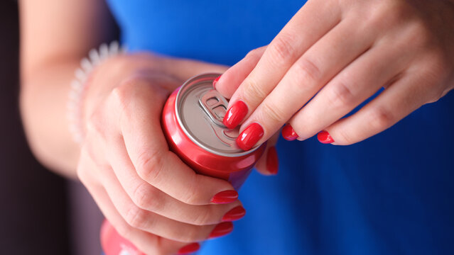 Woman with red manicure opening iron can with drink closeup