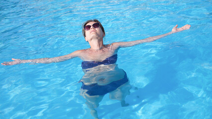 Young woman in sunglasses swimming and relaxing in pool top view