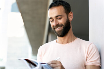 Portrait of smiling latin student studying, learning language, exam preparation, education concept. Handsome bearded hispanic man reading book, taking notes, standing on urban street
