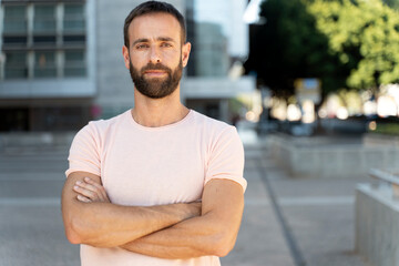 Portrait of pensive handsome hispanic man with arms crossed  looking at camera standing on the street, copy space