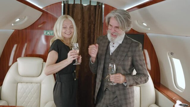 Happy mature rich couple dancing while luxury traveling in private jet plane. Senior man and woman enjoying vip romantic traveling with glasses of champagne, while flying on first class airlines