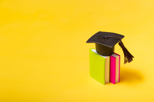 Graduation cap on colorful books on yellow background. Education concept with copy space