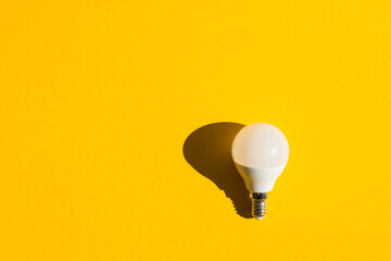 LED light bulb lies on a pastel yellow background. Energy saving concept. Minimalism, top view