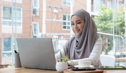 Asian Muslim business woman in hijab headscarf working with computer laptop in the modern office....