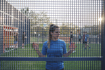 Young female soccer player leaning on net fence on pitch