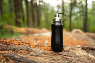 Black metal thermo bottle in the forest