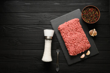 Fototapeta na wymiar Fresh raw meat or ground chicken meat on a wooden cutting board with thyme, spices and garlic. Black wooden background. Top view. Copy space.