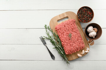 Fototapeta na wymiar Fresh raw meat or ground chicken meat on a wooden cutting board with thyme, spices and garlic. White wooden background. Top view. Copy space.