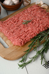 Fresh raw meat or ground chicken meat on a wooden cutting board with thyme, spices and garlic. White wooden background. Top view. Copy space.