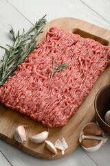 Fresh raw meat or ground chicken meat on a wooden cutting board with thyme, spices and garlic. White wooden background. Top view. Copy space.