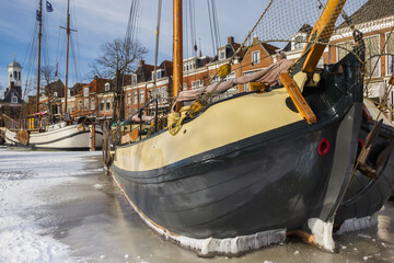 Bow of a historic wooden sailing ship in the frozen canal of Dokkum, Netherlands - obrazy, fototapety, plakaty