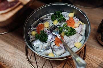 Serving bowl of fresh salty herring with red caviar, onion and green on stand closeup top view. Portion of seasonal appetizer from fish, nutritious dish. Food court, delicious meal, luxurious service