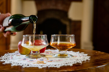 Pouring of apple cider drink in glasses in old french house with fireplace on background, Normandy, France