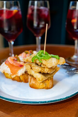 Food and drink in bars of Basque Country and Navarre, pinchos, slices of bread with different toppings fastened with skewers served outdoor with glasses of cold sangria wine, San Sebastian, Spain